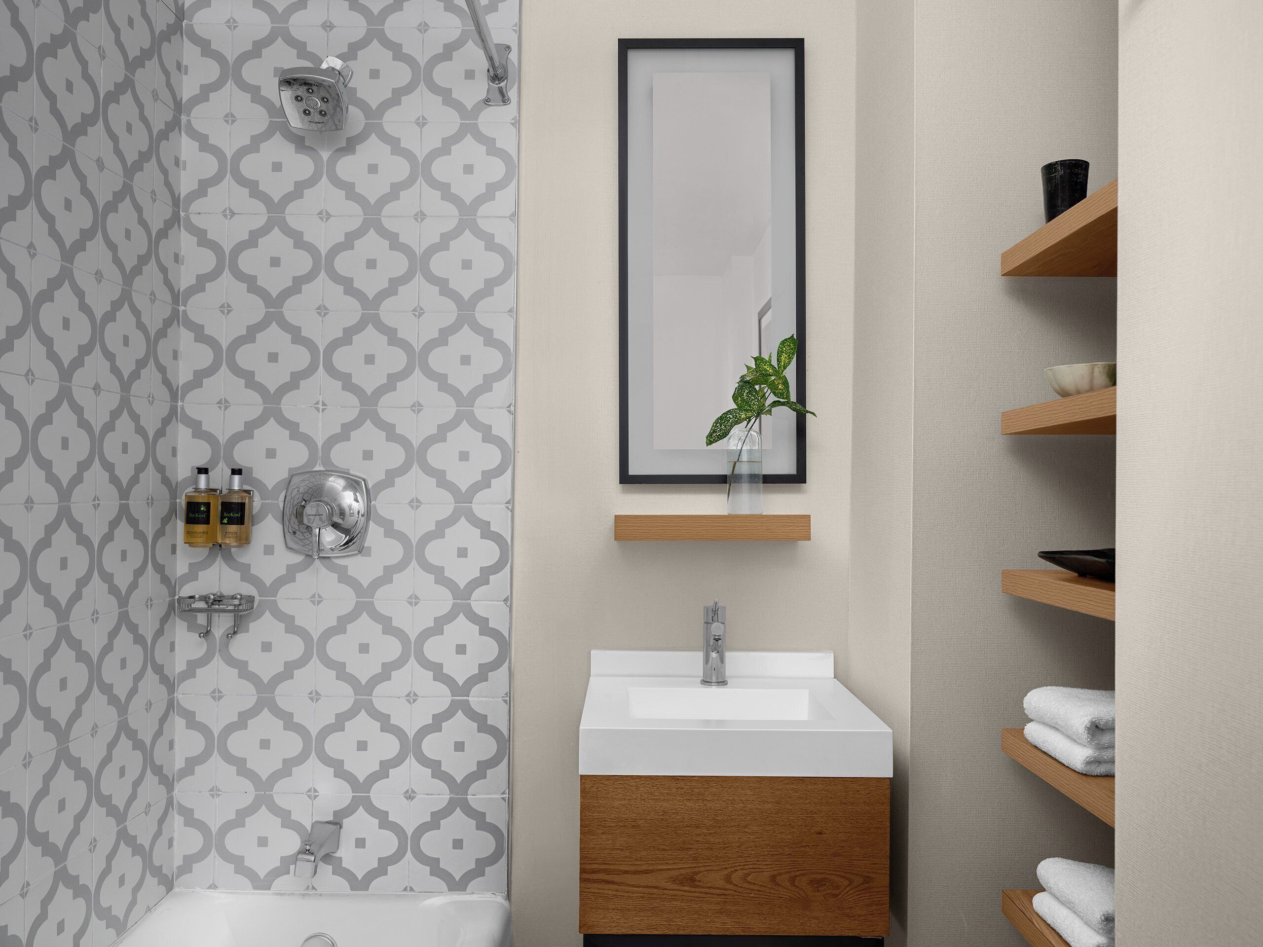 A bathroom with a patterned tile wall, a sink with a wooden cabinet, and a shelf with towels.