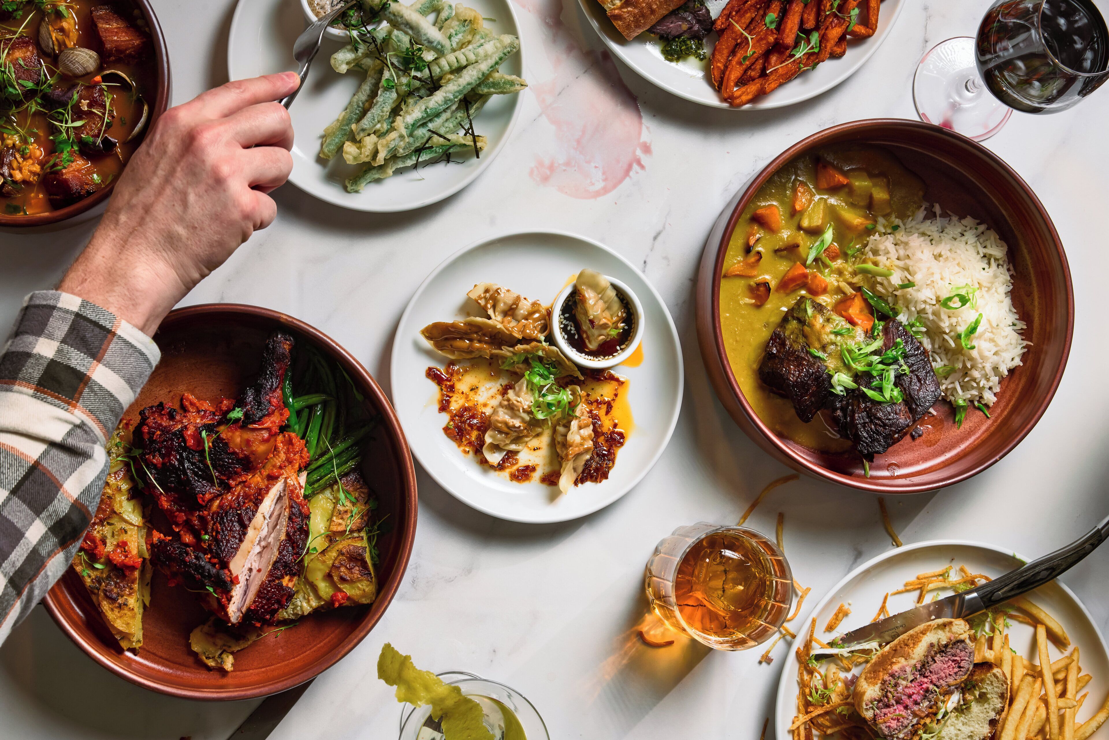 A variety of dishes on a table, including a bowl of rice with vegetables, a plate of dumplings, and a dish with meat.