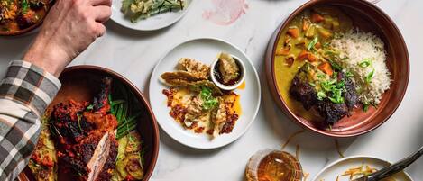 A variety of dishes on a table, including a bowl of rice with vegetables, a plate of dumplings, and a dish with meat.
