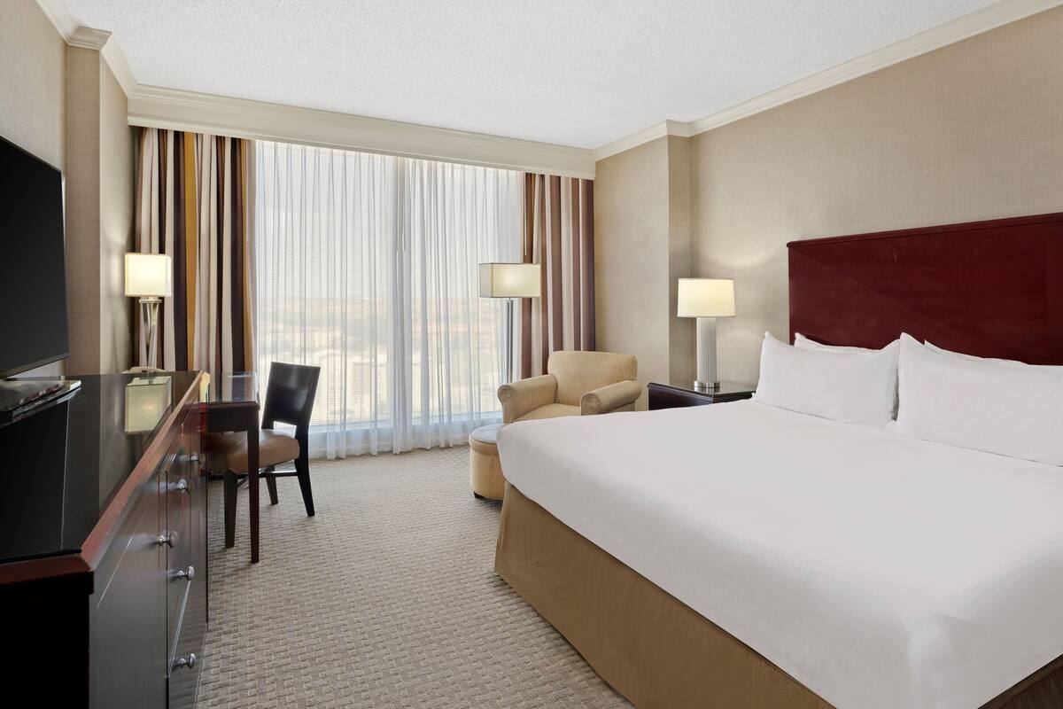 Habitación de hotel con una cama grande, un escritorio con silla, un televisor y una ventana con cortinas.