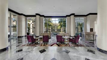 Un vestíbulo amplio con suelo de mármol, ventanas grandes y una mesa de recepción.