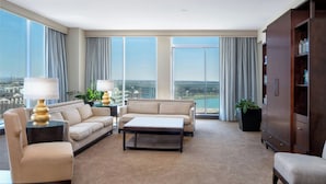A spacious living room with a large sofa set, a coffee table, and a bookshelf. The room has large windows offering a city view. - Renaissance Dallas North Hotel (Farmers Branch)