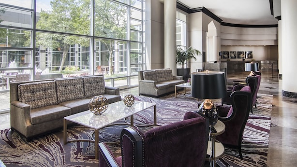 A spacious lobby with a large window, a sofa, a coffee table, and a lamp. - Renaissance Dallas North Hotel (Farmers Branch)