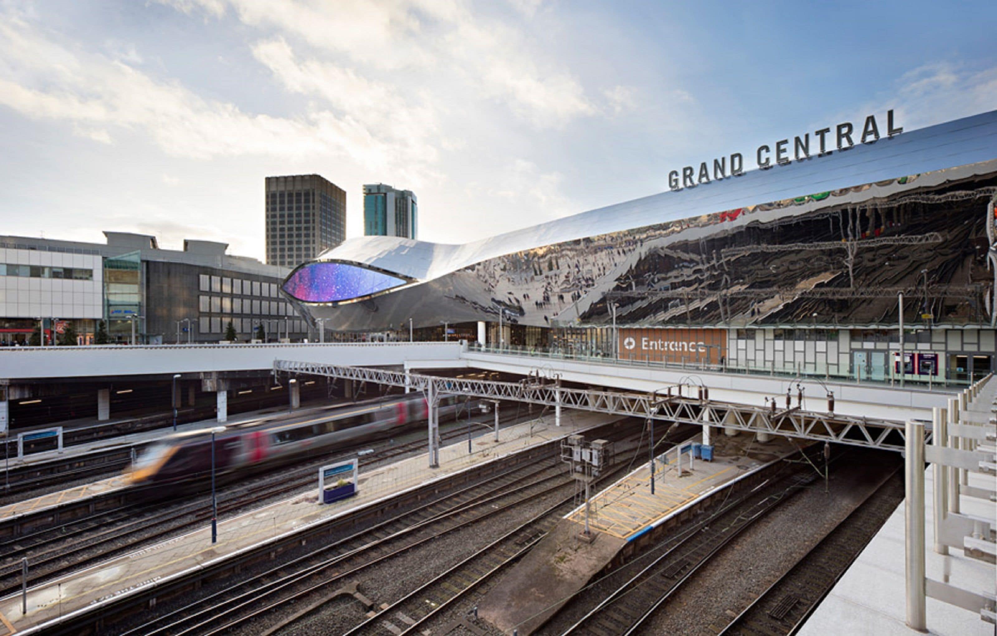 Een modern treinstation met meerdere perrons en sporen, met een opvallend architectonisch ontwerp en een groot, gebogen dak.