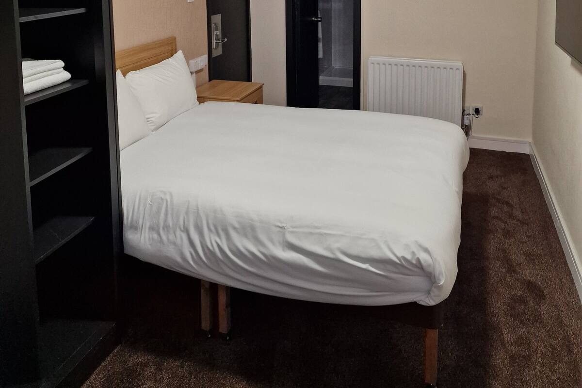 Habitación de hotel con cama, armario, radiador y zona de ducha.