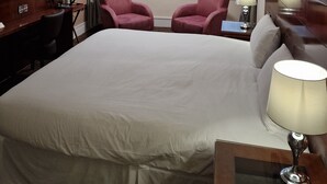 A hotel room with a large bed, two armchairs, a desk with a TV, and a window with curtains.