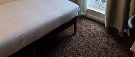 Hotellihuone, jossa on yksi sänky, seinällä kehystetty taulu ja ikkunasta avautuva näkymä kaupunkiin.