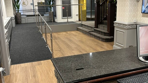 A spacious lobby with a wooden floor, a staircase, and a reception desk with a computer monitor.