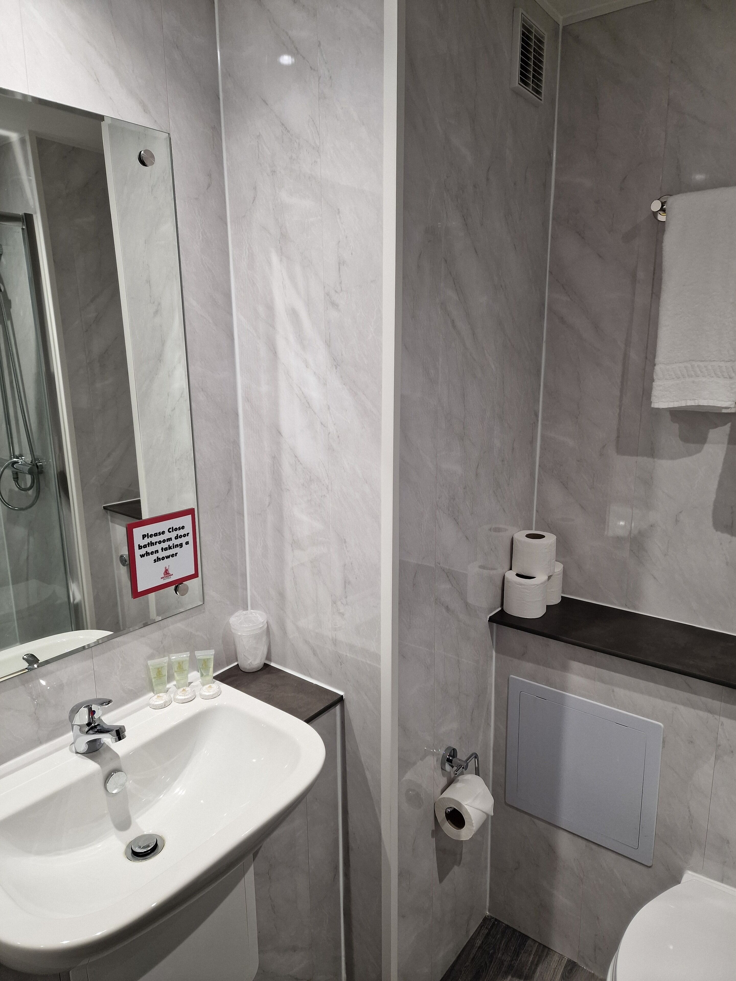 A modern bathroom with a sink, toilet, and shower. A sign instructs to close the bathroom door when taking a shower.