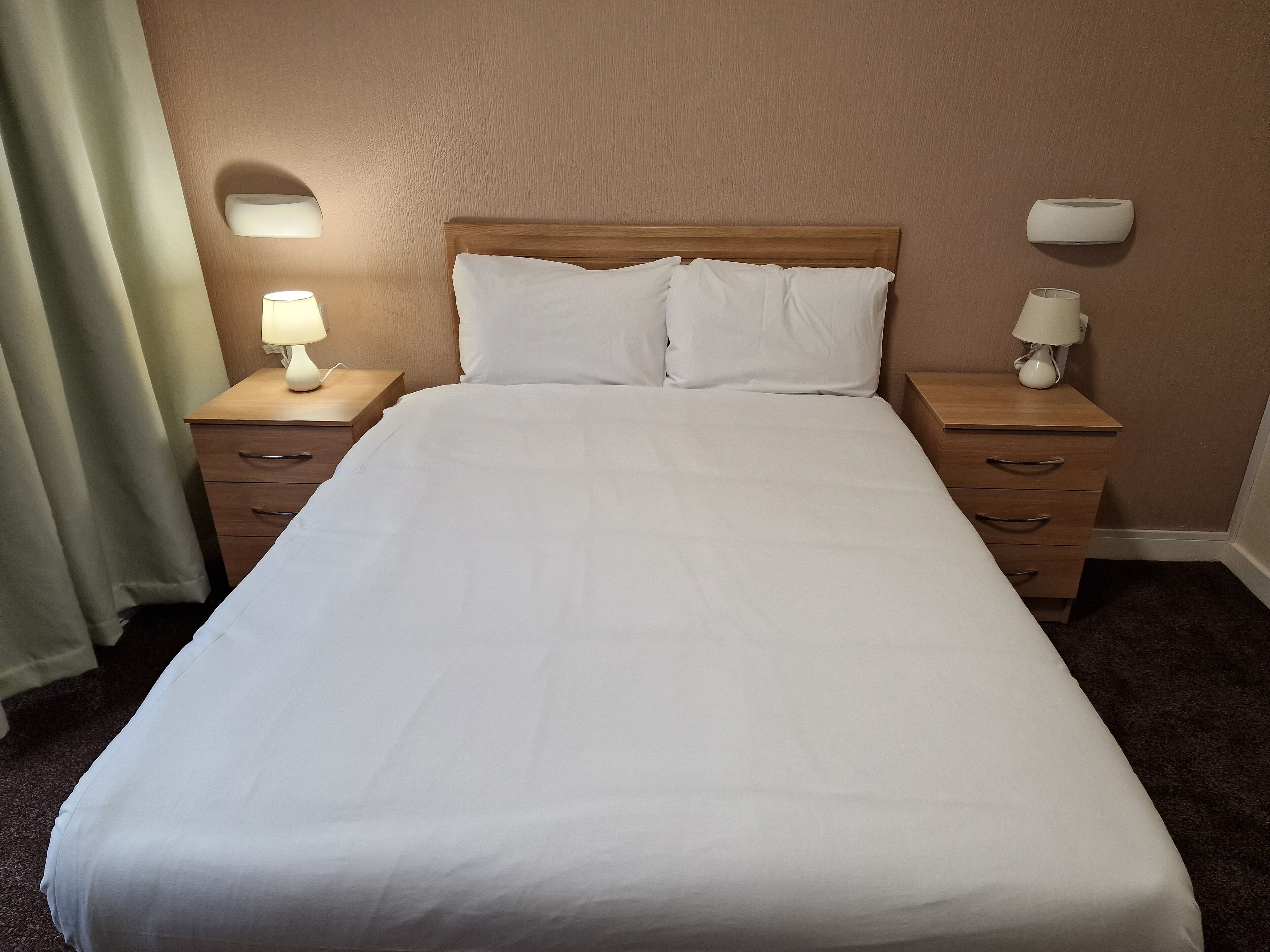 A neatly made bed with white linens, two bedside tables with lamps, and a wooden headboard.