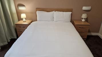 Una cama bien tendida con sábanas blancas, dos mesitas de noche con lámparas y un cabecero de madera.