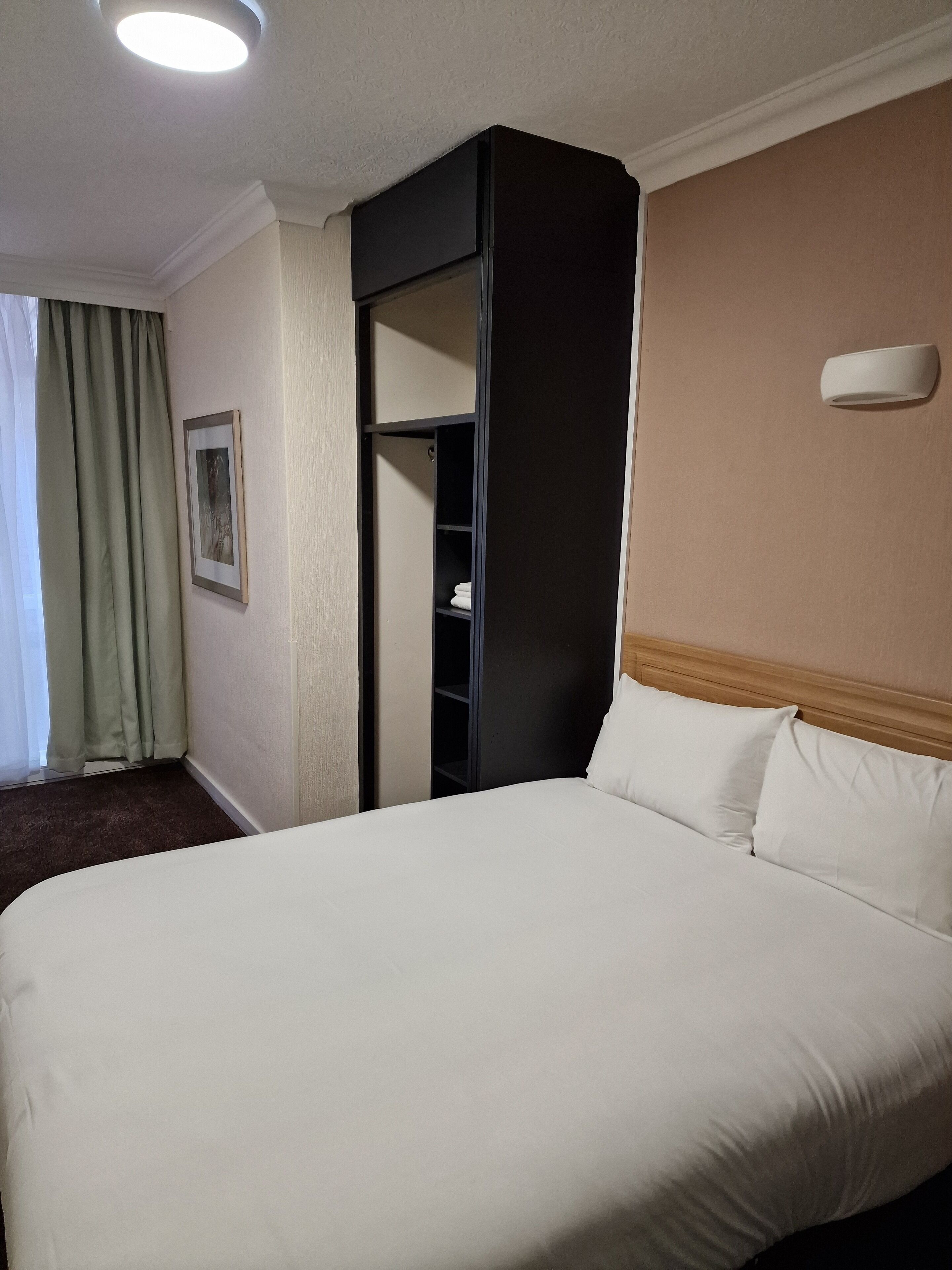 Una camera d'albergo con un letto grande, un armadio, un quadro appeso al muro e una finestra con tende.