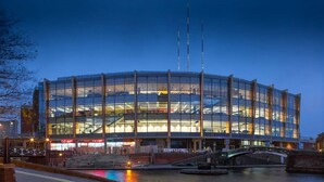 A modern, multi-story building with a glass facade, surrounded by water and a bridge.