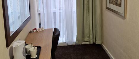 Habitación de hotel con un escritorio de madera, un cuadro enmarcado en la pared, una ventana con cortinas translúcidas y piso alfombrado.