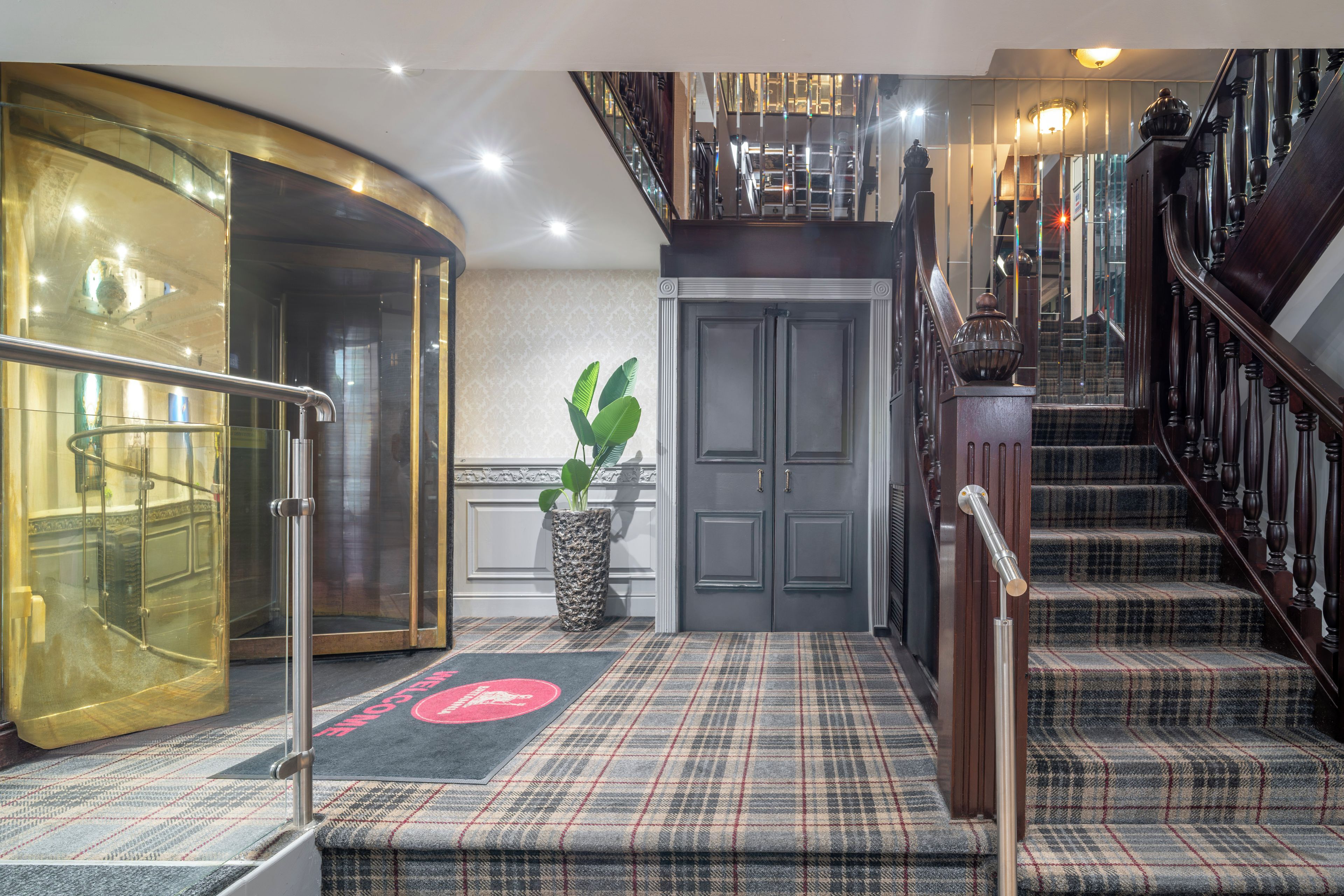 A hotel lobby with a grand staircase, a reception desk, and a large potted plant.