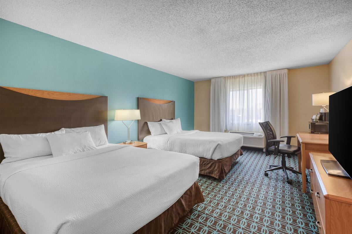 A hotel room with two beds, a desk, a chair, a TV, and a window with curtains.
