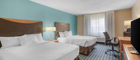Quarto de hotel com duas camas, uma escrivaninha, uma cadeira, televisão e janela com cortinas.