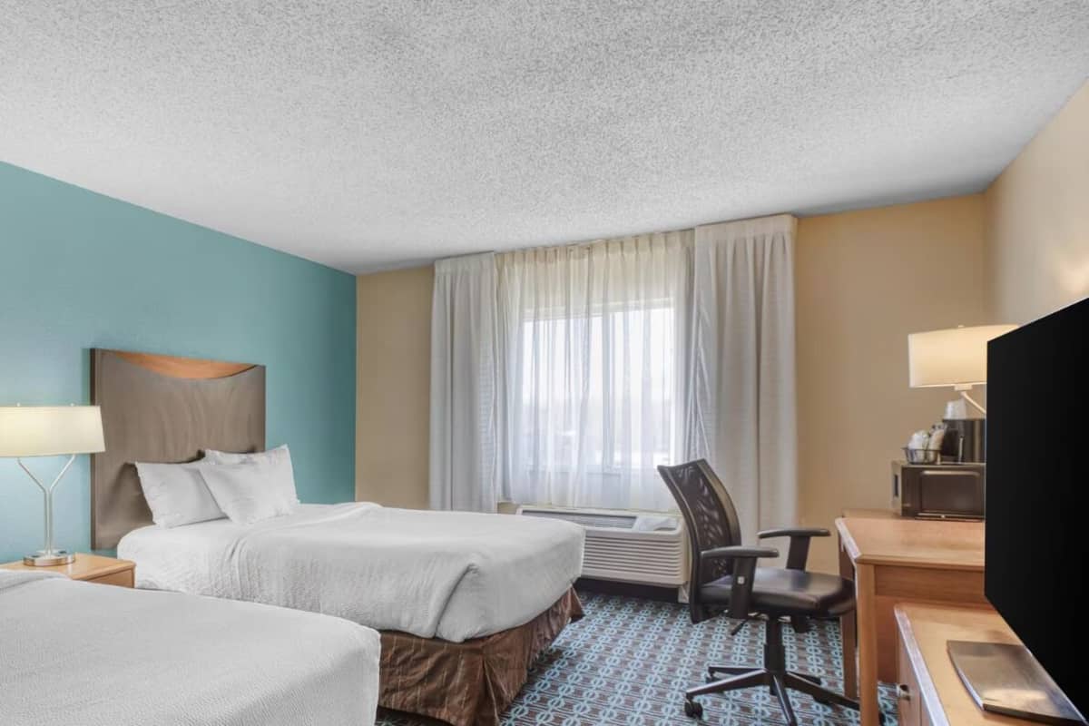 A hotel room with two beds, a desk, a chair, a TV, and a window with curtains.