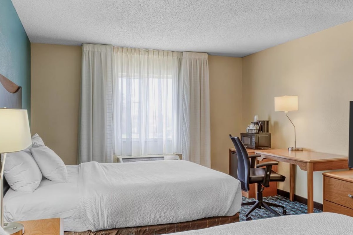 A hotel room with two beds, a desk with a computer, a TV, and a lamp.