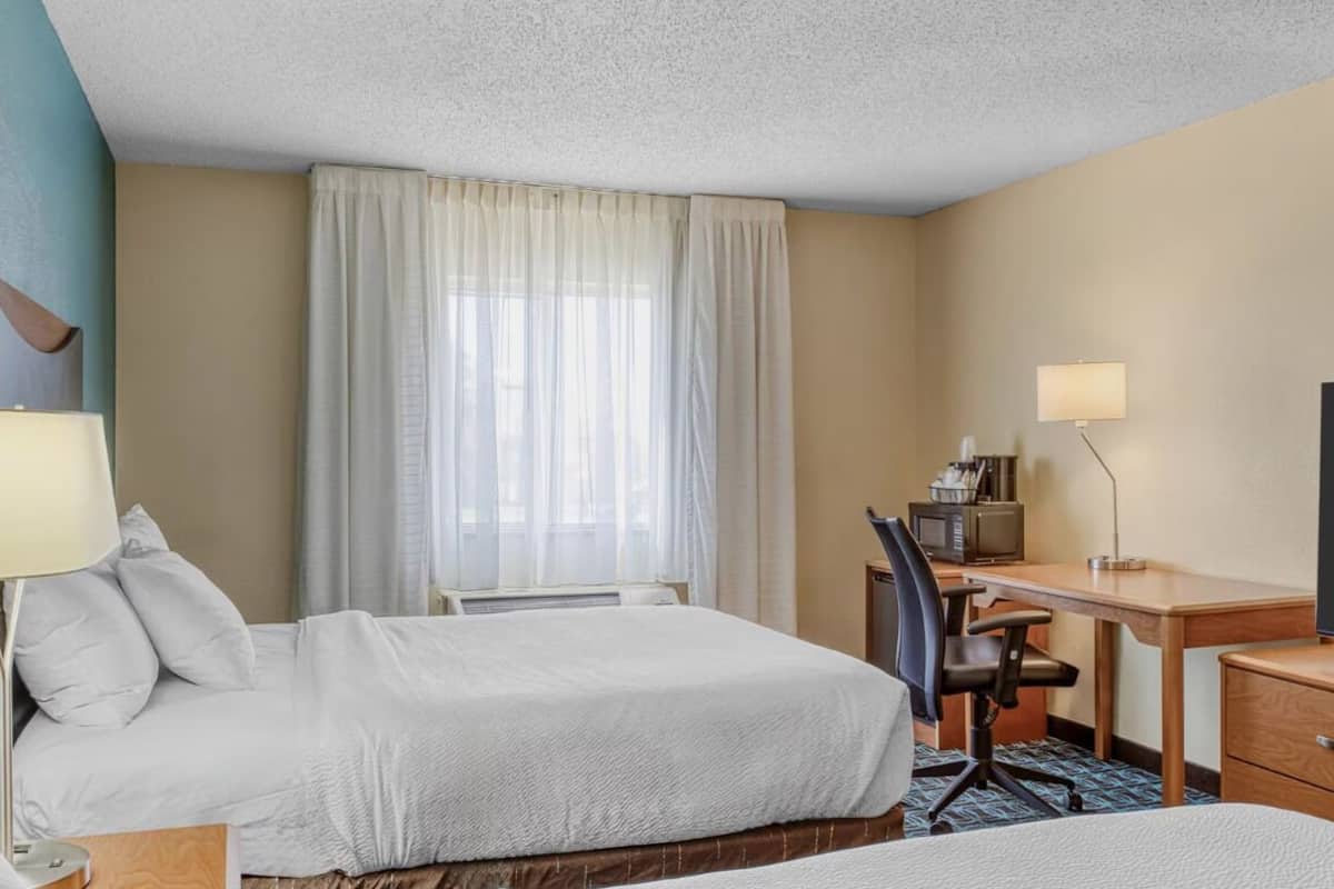 A hotel room with two beds, a desk with a computer, a TV, and a lamp.