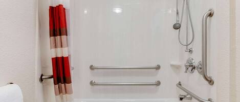 Un baño con bañera, ducha y barras de apoyo.