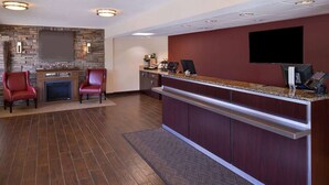 Un vestíbulo de hotel con mostrador de recepción, dos sillones rojos, una chimenea y un televisor en la pared.