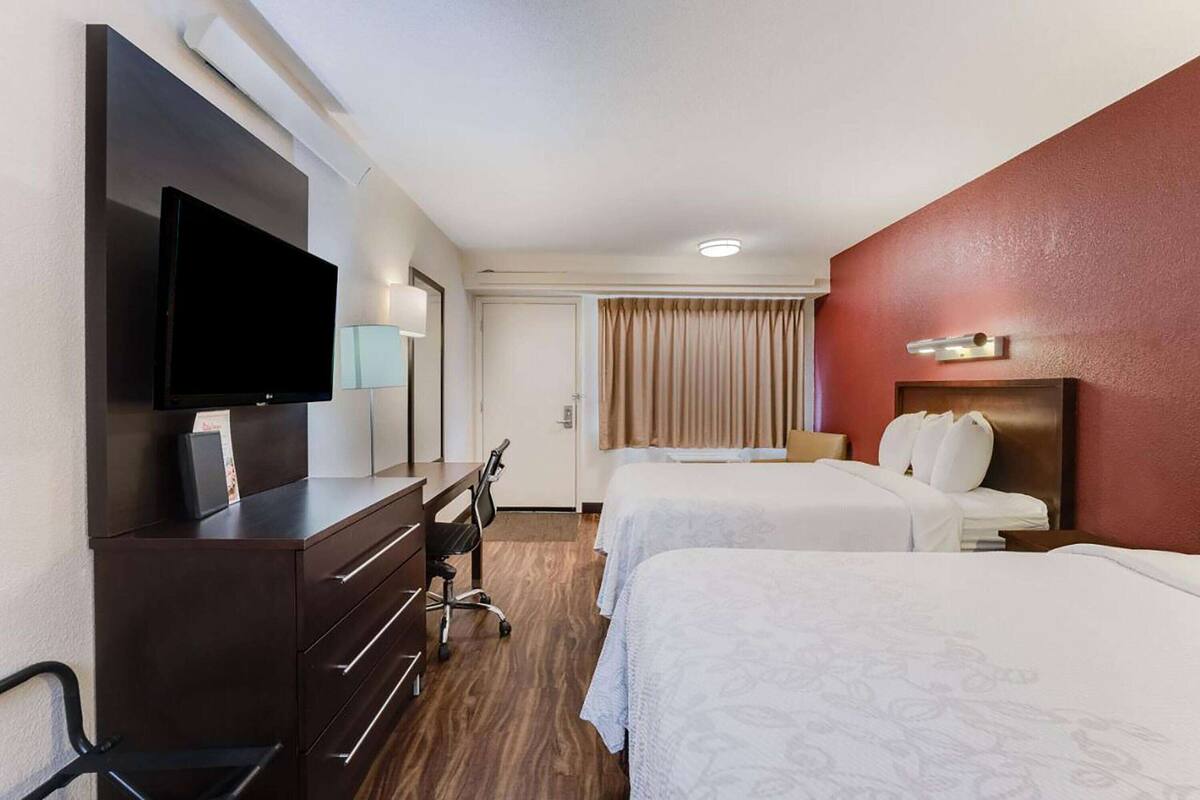 Une chambre d’hôtel avec deux lits, un bureau doté d’un téléviseur à écran plat, une commode et une fenêtre avec des rideaux.