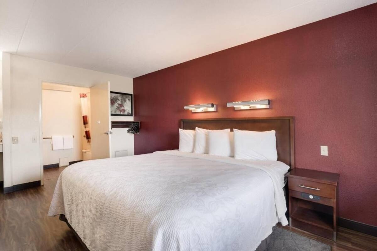 Une chambre d’hôtel avec un grand lit, une table de chevet en bois, un luminaire fixé au mur et une porte donnant sur une salle de bain.