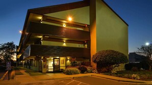 Un edificio moderno con techo plano, ventanas grandes y un estacionamiento.