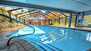 Una piscina con agua azul cristalina, rodeada de sillas de descanso y un área techada.
