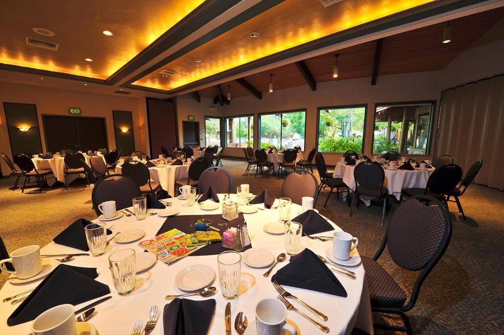 A conference room with round tables set for dining, equipped with chairs, plates, cutlery, and glasses.