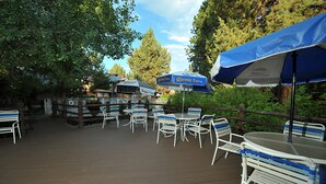 Un patio al aire libre con mesas, sillas, sombrillas y una terraza de madera.