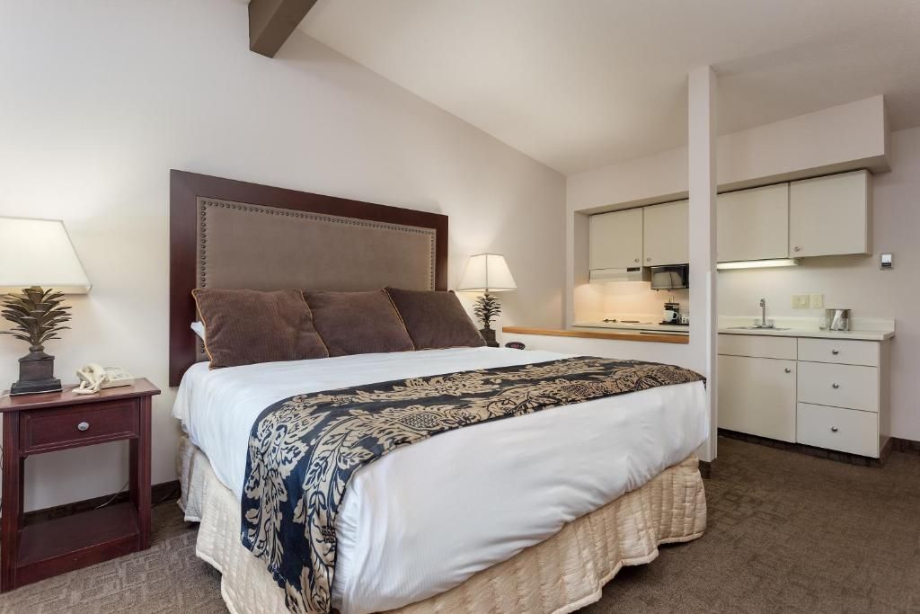 A hotel room with a large bed, bedside tables, a desk, a mirror, and a kitchenette.