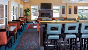 A hotel lobby with a fireplace, a TV, and a bar area. - PrimeStay Extended Suites by IHG (Madison)