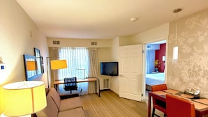 A hotel room with a sofa, a dining table, a TV, and a door leading to a balcony. - PrimeStay Extended Suites by IHG (Madison)