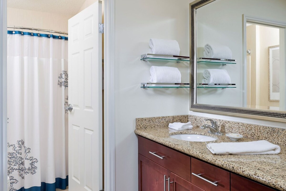 A bathroom with a shower curtain, a sink, a mirror, and glass towel holders.