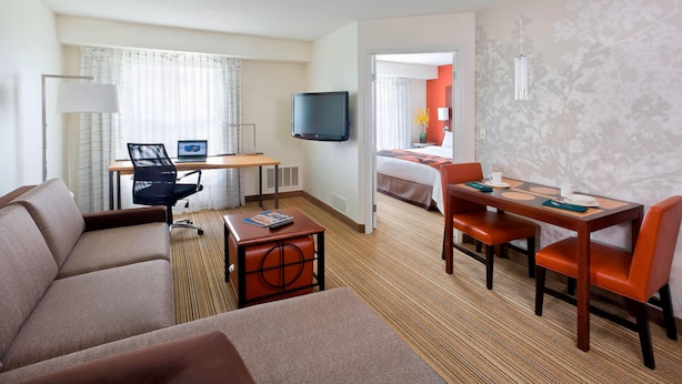 A hotel room with a sofa, a desk with a computer, a TV, a dining table with chairs, and a bed. - PrimeStay Extended Suites by IHG (Madison)