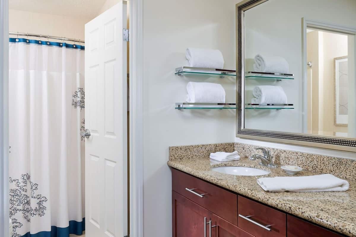 A bathroom with a shower curtain, a sink, a mirror, and glass towel holders.
