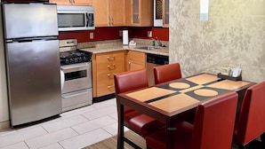 A modern kitchen with stainless steel appliances, wooden cabinets, and a dining area with red chairs. - PrimeStay Extended Suites by IHG (Madison)