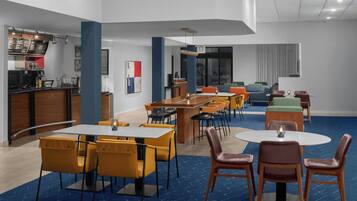A modern dining area with multiple tables and chairs, a bar counter, and a seating area with sofas.