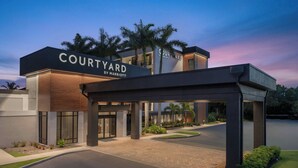 Entrada de un hotel Courtyard by Marriott, con un paseo techado, palmeras y zonas ajardinadas.