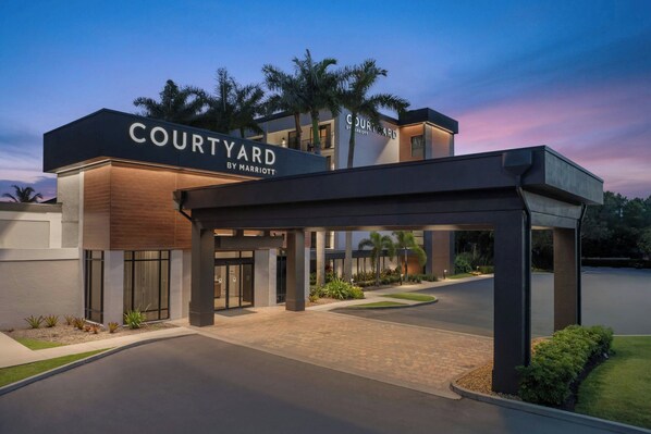 A Courtyard by Marriott hotel entrance with a covered walkway, palm trees, and a landscaped area.