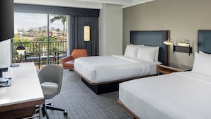 Habitación de hotel con una cama grande, un escritorio, una silla y un balcón con vistas a la ciudad.