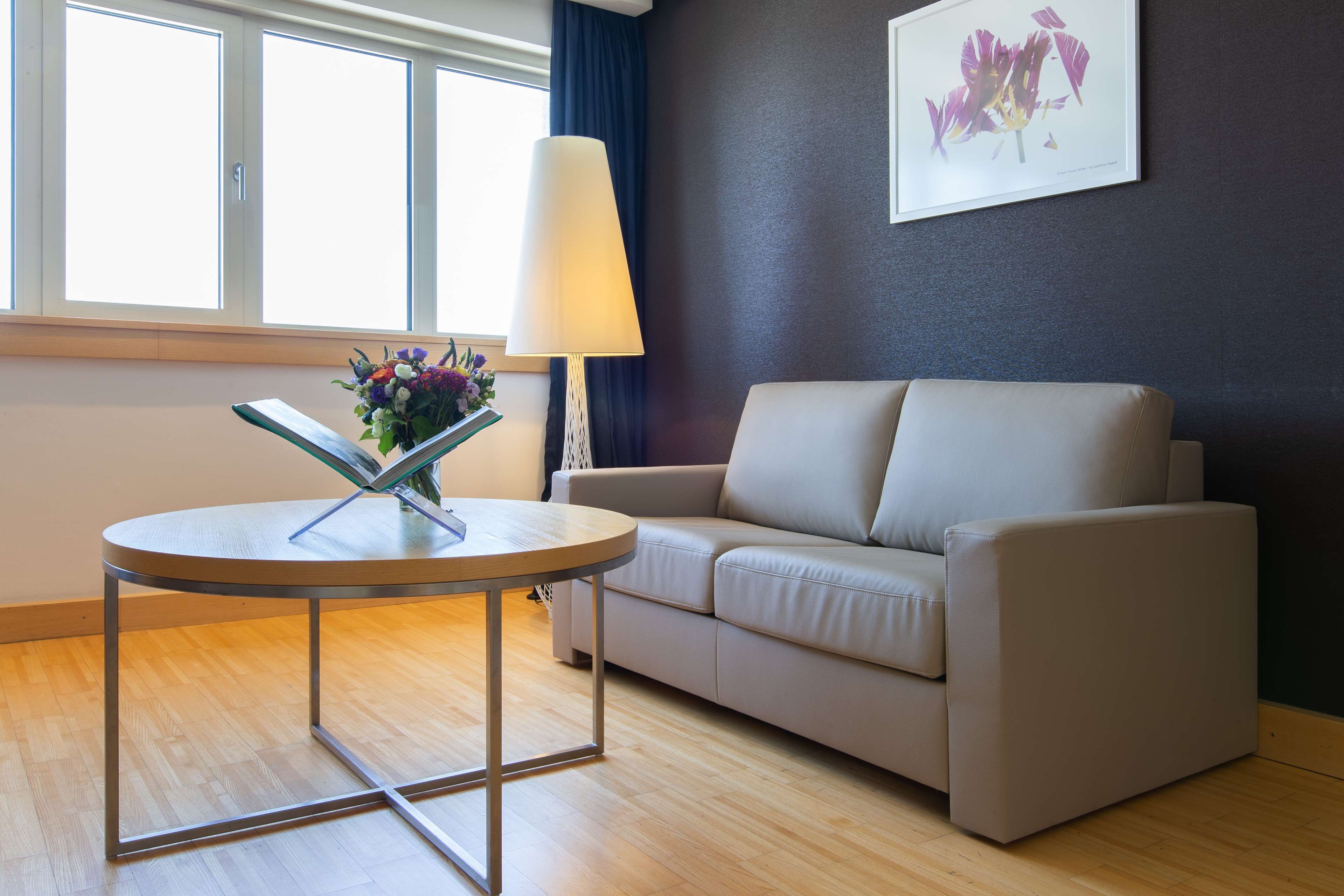 A modern living room with a round table, a beige sofa, a floor lamp, and a window with curtains.