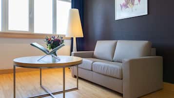 A modern living room with a round table, a beige sofa, a floor lamp, and a window with curtains.