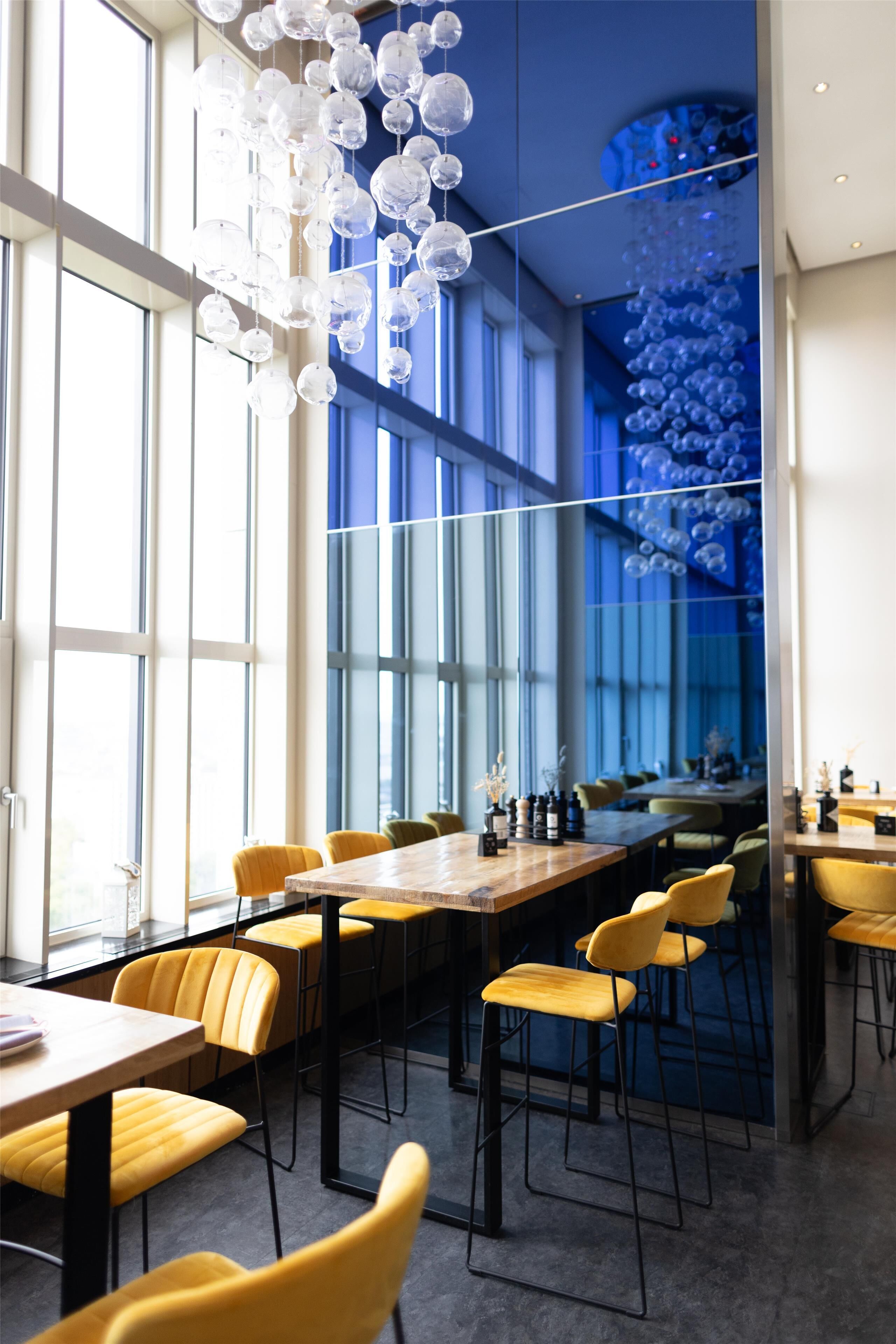 A modern dining area with high ceilings, large windows, and a central chandelier.