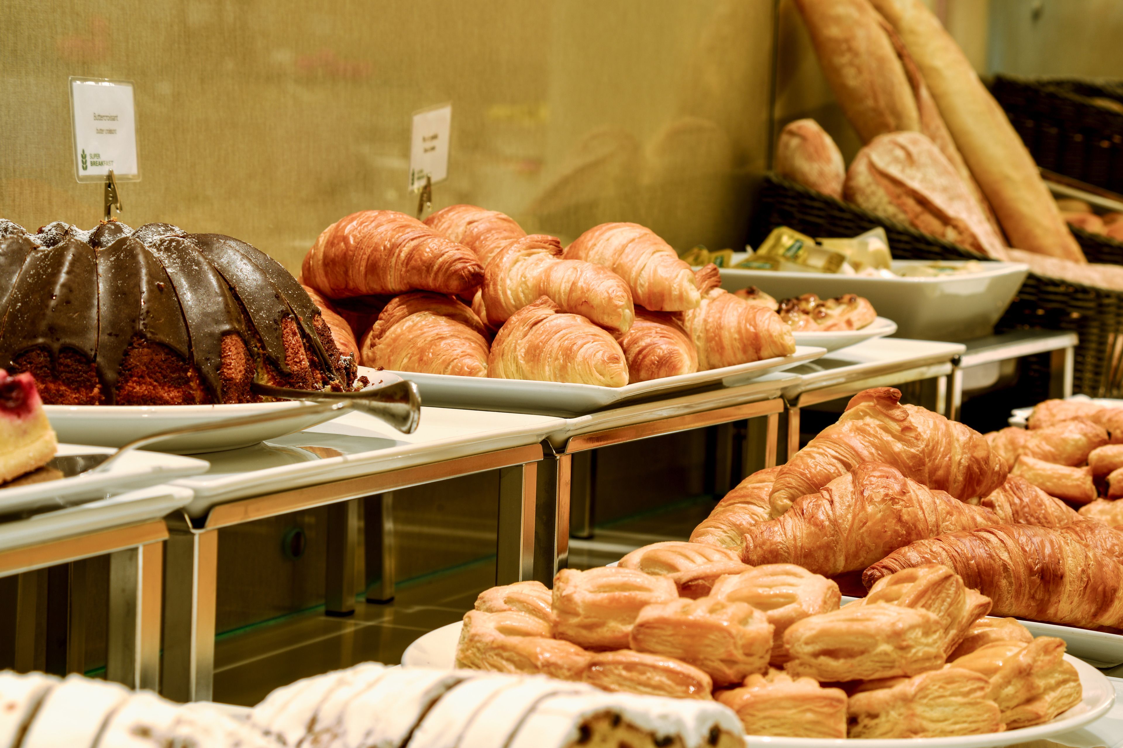 Un bufé con diversas opciones de repostería, incluyendo un pastel bundt de chocolate, croissants y otras delicias.