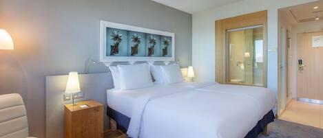 Una habitación de hotel moderna con una cama grande, una mesita de noche de madera, una lámpara de escritorio y una obra de arte en la pared.