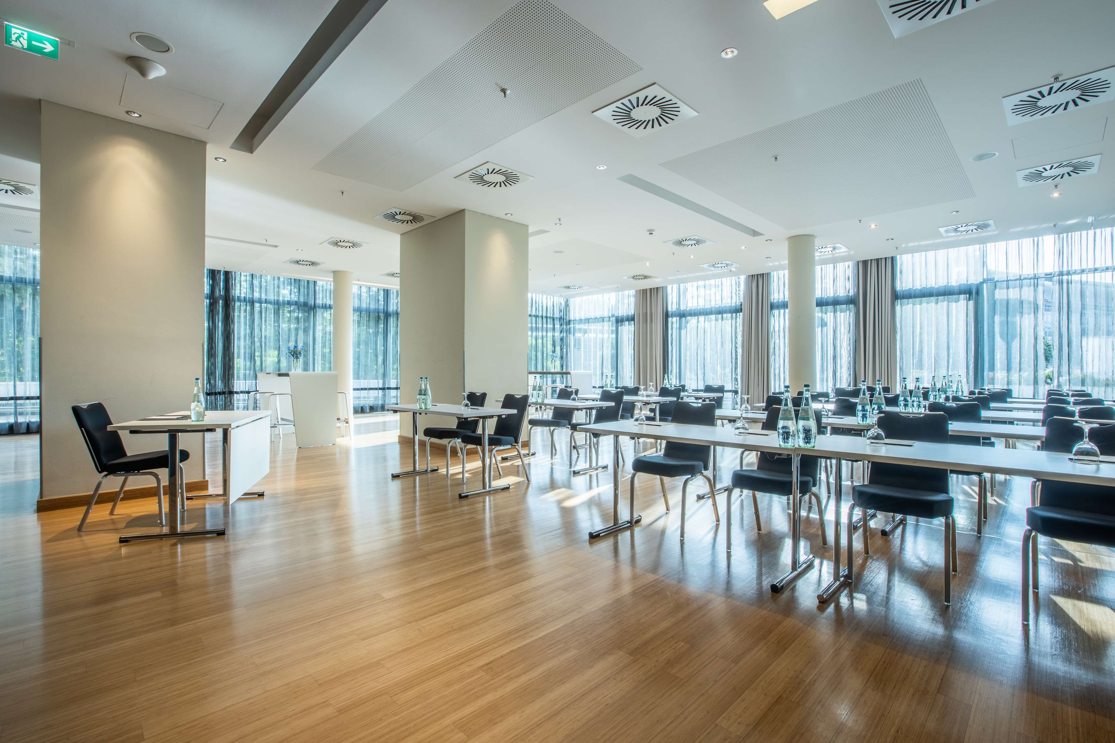 Een ruime vergaderzaal met lange tafels, stoelen en een modern plafondontwerp.