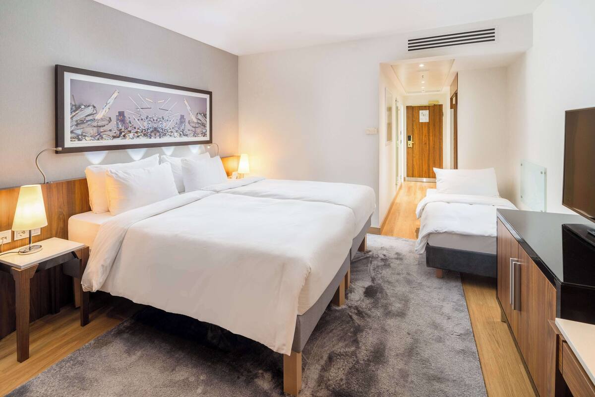 A hotel room with a large bed, a desk with a lamp, a TV, and a painting on the wall.